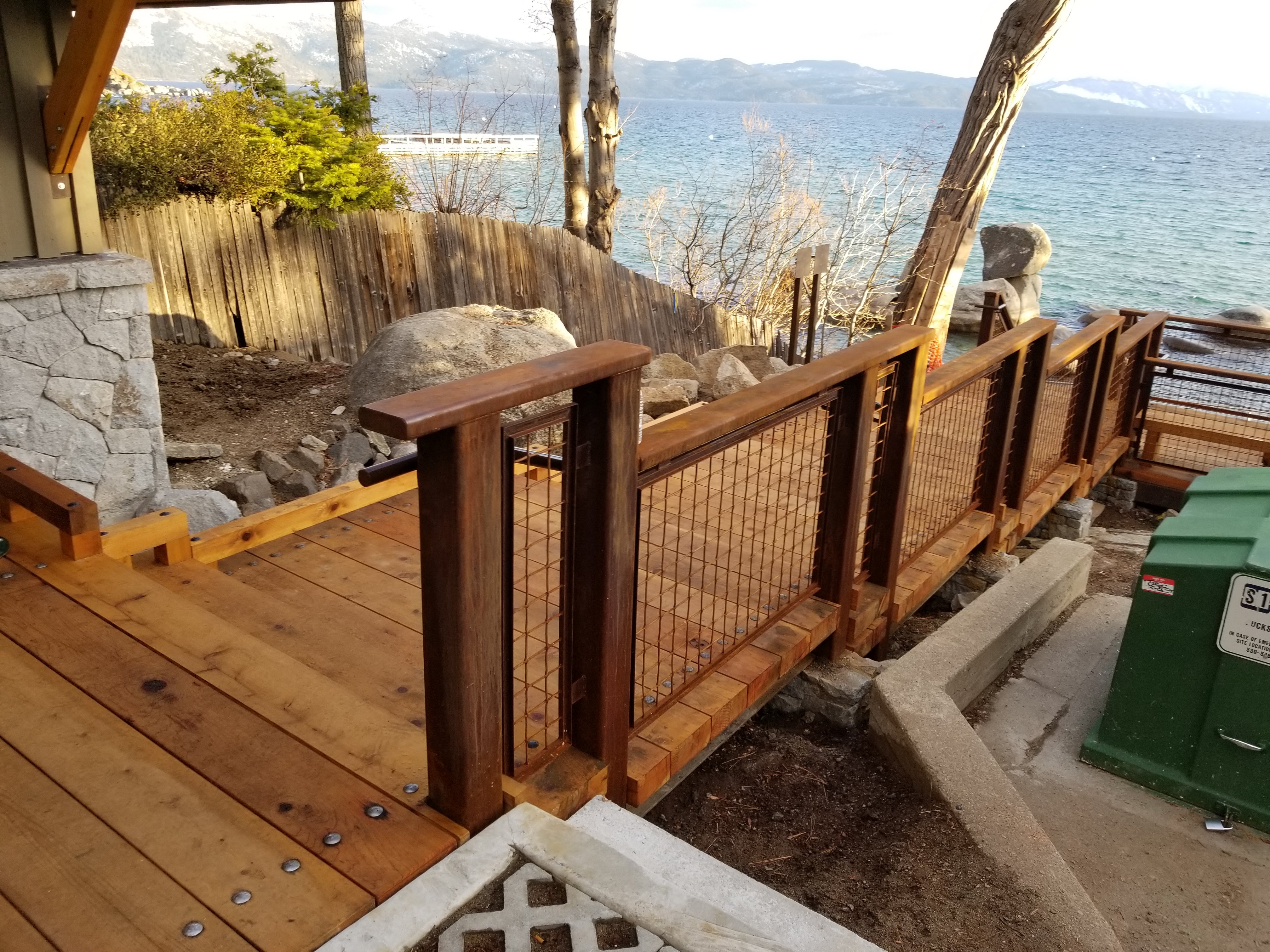 Finished timber deck with steel-mesh guardrail beside a lake