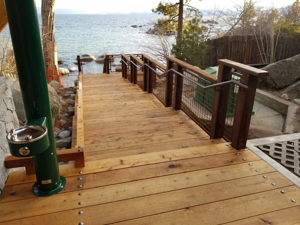 Wood stairs and walkway with steel mesh guardrail beside a lake
