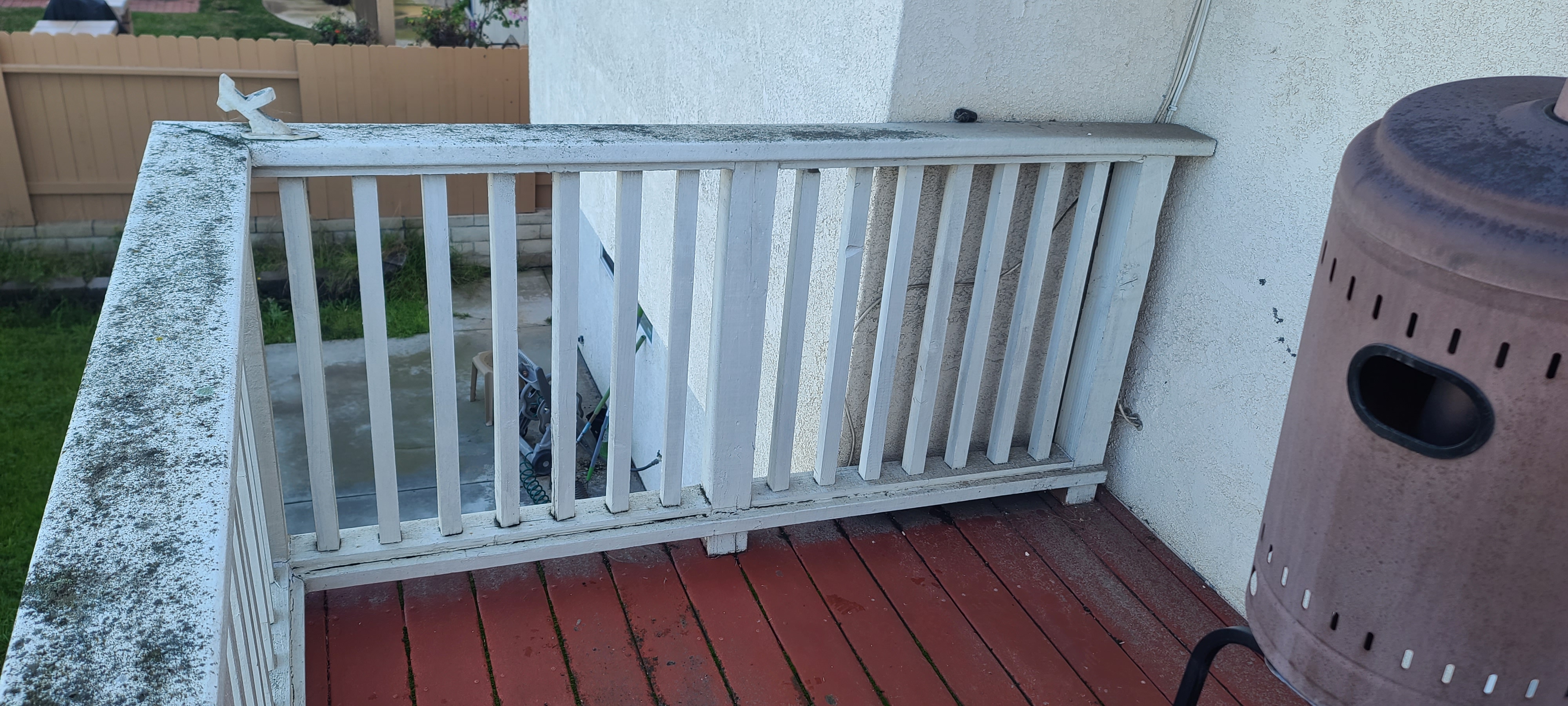 Wood balcony guardrail with weathered, moss-covered top rail above a red-painted deck