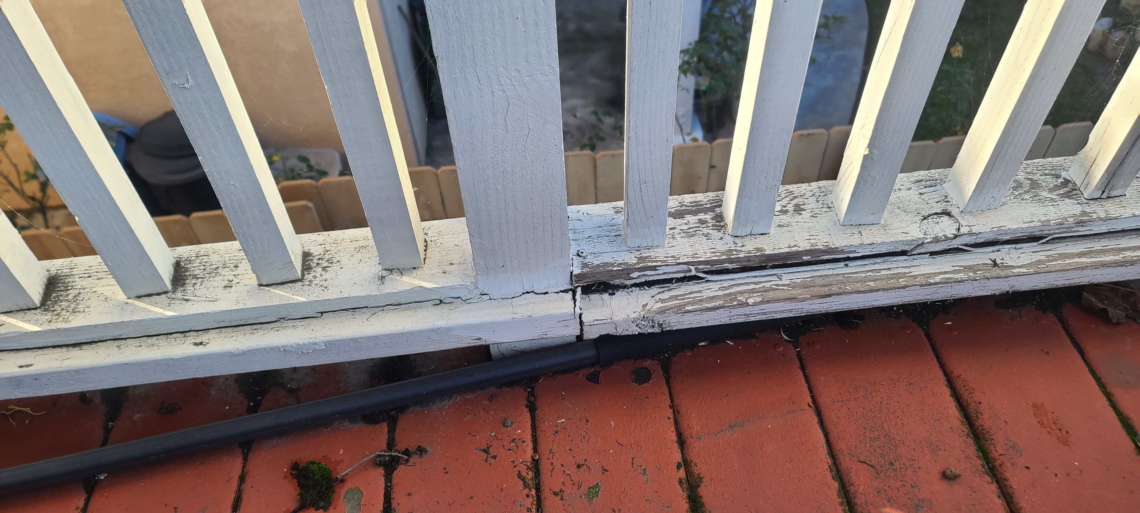 Close-up of a balcony railing base with cracked, deteriorated wood